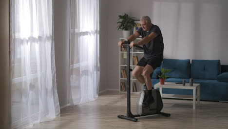 Mann-Mittleren-Alters-Trainiert-Auf-Dem-Heimtrainer-Im-Wohnzimmer,-Achtet-Auf-Seine-Gesundheit-Und-Verliert-An-Gewicht,-Bleibt-Fit-Bei-Sportlicher-Aktivität